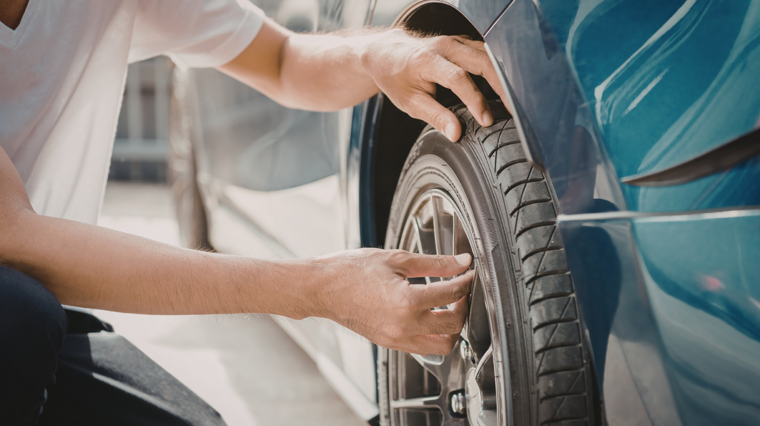 Pessoa realizando vistoria no pneu de um carro, verificando a banda de rodagem com as mãos. Prossegue vistoria veiuclar na paraíba. vistoria de carro na paraiba