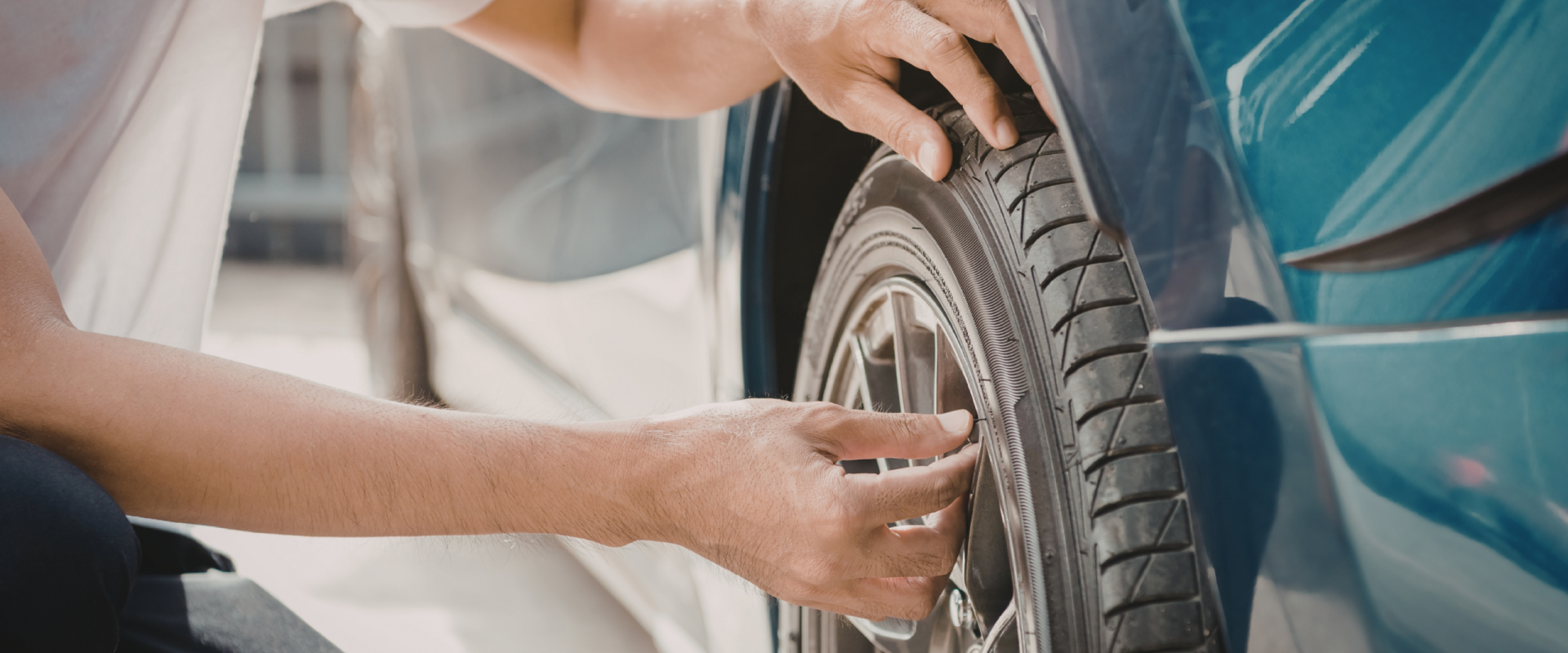 Pessoa realizando vistoria no pneu de um carro, verificando a banda de rodagem com as mãos. Prossegue vistoria veiuclar na paraíba. vistoria de carro na paraiba